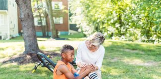 A woman comforts an injured child beside a bicycle in a sunny park setting.