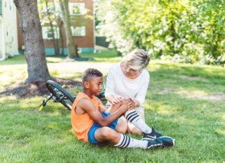 A woman comforts an injured child beside a bicycle in a sunny park setting.