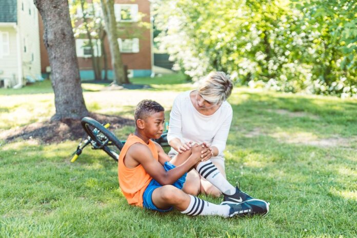 A woman comforts an injured child beside a bicycle in a sunny park setting. A woman comforts an injured child beside a bicycle in a sunny park setting.