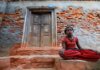Детская бедность в Канаде удвоилась с 2020 года — доклад ЮНИСЕФ A young girl sits calmly by a rustic brick wall with a wooden doorway, conveying resilience and tranquility.