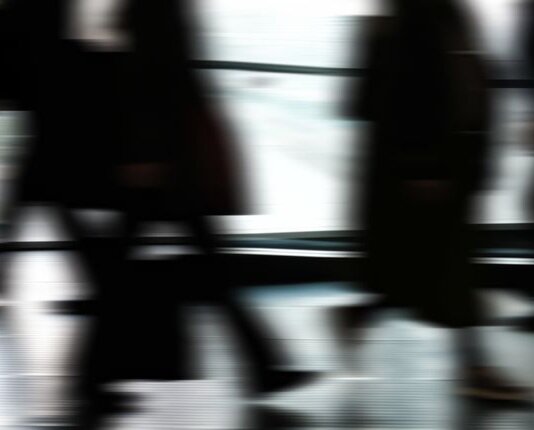 Abstract blurred motion of people walking indoors, depicting urban life and busy routines.