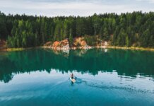Места для каякинга с прокатом в Трай-Ситис, куда легко добраться на транспорте Aerial shot of a woman paddle boarding on a serene lake in Rezh, Russia, surrounded by lush greenery.