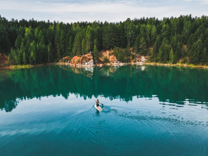 Aerial shot of a woman paddle boarding on a serene lake in Rezh, Russia, surrounded by lush greenery.