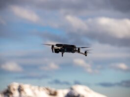 Aerial view of a drone flying over snow-covered mountains with dramatic clouds.