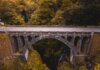 Когда Карни преодолеет пропасть между словами и делами? Aerial view of a historic stone bridge in Madeira, surrounded by lush greenery and dramatic landscapes.