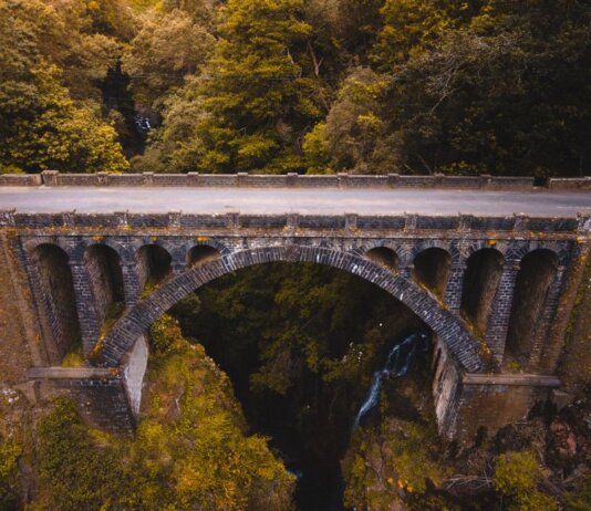 Aerial view of a historic stone bridge in Madeira, surrounded by lush greenery and dramatic landscapes.