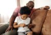 В Threads появятся инструменты родительского контроля African American father and son bonding indoors while playing on smartphone. Capturing family leisure moments.