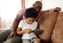 African American father and son bonding indoors while playing on smartphone. Capturing family leisure moments.