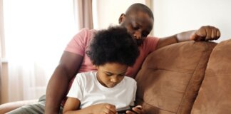 African American father and son bonding indoors while playing on smartphone. Capturing family leisure moments.