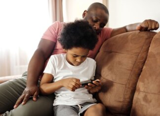 African American father and son bonding indoors while playing on smartphone. Capturing family leisure moments.