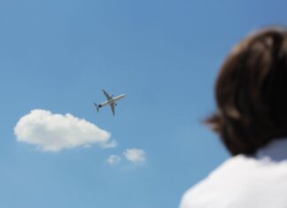 An airplane flies high in a clear sky while a person watches from below.