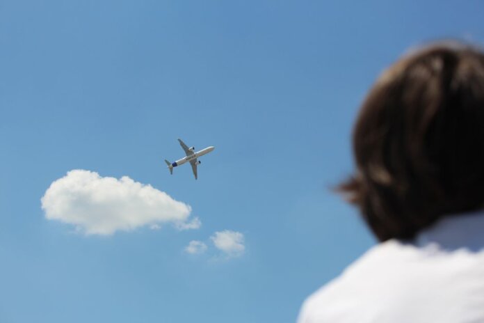 An airplane flies high in a clear sky while a person watches from below. An airplane flies high in a clear sky while a person watches from below.