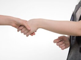 An up-close image of two people shaking hands in a professional setting against a white background.