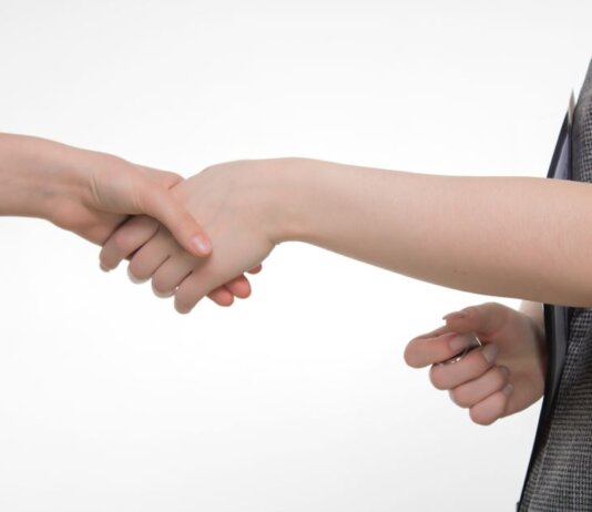 An up-close image of two people shaking hands in a professional setting against a white background.