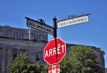 Bilingual street signs with stop sign against a clear blue sky in a city setting, featuring historical street names.