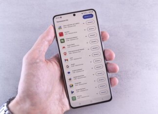 Close-up of a hand holding a smartphone displaying app updates on a light background.