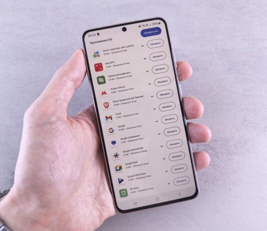 Close-up of a hand holding a smartphone displaying app updates on a light background.