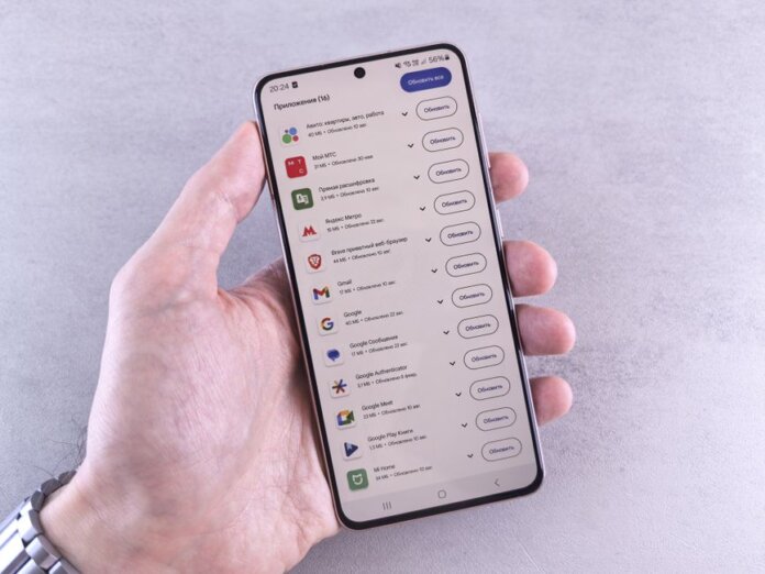 Close-up of a hand holding a smartphone displaying app updates on a light background. Close-up of a hand holding a smartphone displaying app updates on a light background.
