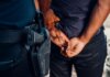 Подросток арестован в Боуманвилле по делу о стрельбе в Ошаве Close-up of a police officer arresting a suspect with visible firearm outdoors.