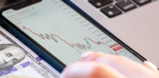Close-up of a smartphone displaying stock market data over a dollar bill on a desk.