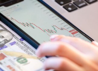 Университет Западного Онтарио получил 9,8 млн долларов на исследования Close-up of a smartphone displaying stock market data over a dollar bill on a desk.