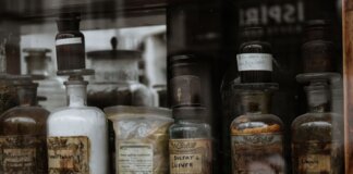 Collection of vintage apothecary bottles with handwritten labels on a wooden shelf, reflecting a medieval charm.