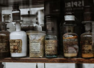 Collection of vintage apothecary bottles with handwritten labels on a wooden shelf, reflecting a medieval charm.