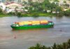Colorful container ship sailing on a river near a small town, view from above.