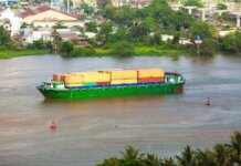 Colorful container ship sailing on a river near a small town, view from above.