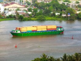 Colorful container ship sailing on a river near a small town, view from above.