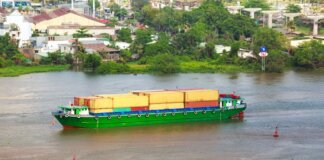 Colorful container ship sailing on a river near a small town, view from above.