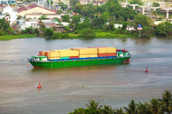 Colorful container ship sailing on a river near a small town, view from above.