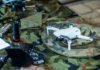 Министр МакГинти объявил о производстве дронов в Квебеке Compact white drone on camouflage gear, surrounded by flashlight and tools.