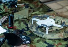Министр МакГинти объявил о производстве дронов в Квебеке Compact white drone on camouflage gear, surrounded by flashlight and tools.