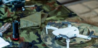 Compact white drone on camouflage gear, surrounded by flashlight and tools.