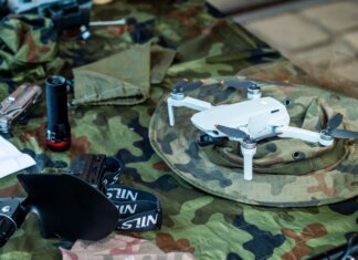 Compact white drone on camouflage gear, surrounded by flashlight and tools.