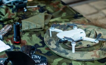 Министр МакГинти объявил о производстве дронов в Квебеке Compact white drone on camouflage gear, surrounded by flashlight and tools.