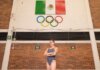 Олимпийские чемпионы выступят за Канаду на Играх Содружества 2026 Confident female athlete in swimsuit poses below Mexican flag and Olympic rings indoors.