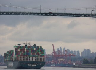 Container ship traverses under Lions Gate Bridge with Vancouver skyline backdrop, showcasing logistics and transport.