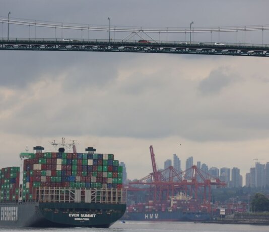 Container ship traverses under Lions Gate Bridge with Vancouver skyline backdrop, showcasing logistics and transport.