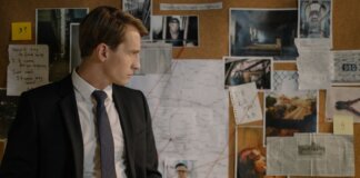 Detective in suit examining evidence on cork board during investigation process.
