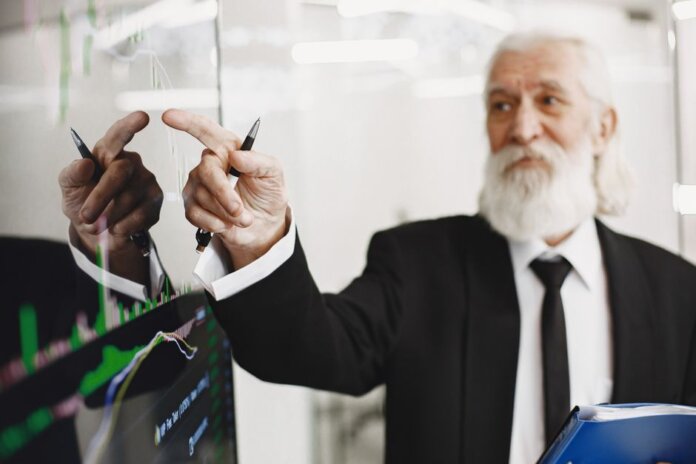Elderly businessman with beard presenting financial trends on a screen. Elderly businessman with beard presenting financial trends on a screen.