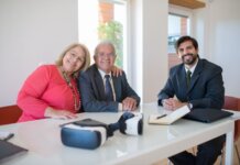 Elderly couple smiling with real estate agent during home meeting, showcasing modern technology.