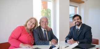 Elderly couple smiling with real estate agent during home meeting, showcasing modern technology.