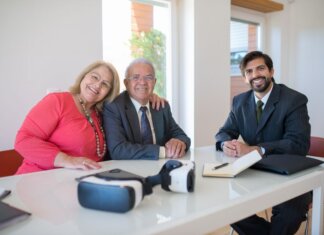 Ньюфаундленд и Лабрадор принимают заявки на субсидии на отопление Elderly couple smiling with real estate agent during home meeting, showcasing modern technology.
