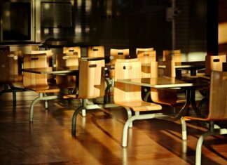 Национальная программа школьного питания набирает обороты в Канаде Empty wooden chairs and tables in a sunlit cafeteria setting, casting dramatic shadows.