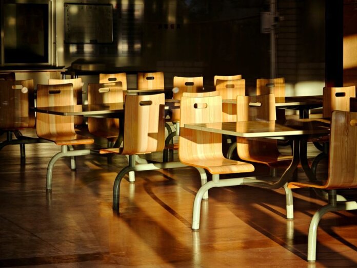 Empty wooden chairs and tables in a sunlit cafeteria setting, casting dramatic shadows. Empty wooden chairs and tables in a sunlit cafeteria setting, casting dramatic shadows.