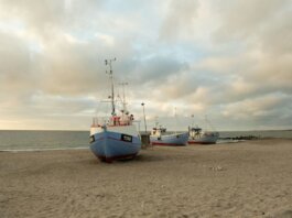 Fishing boats anchored on the sandy shores of Thisted, Denmark during a calm sunset.
