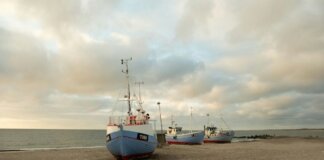 Fishing boats anchored on the sandy shores of Thisted, Denmark during a calm sunset.