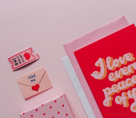 Flat lay of romantic cards and envelopes with love messages on a soft pink background.